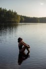 Зверху тонка жінка в купальнику сидить із закритими очима у спокійній воді озера, насолоджуючись заходом сонця та величними пейзажами — стокове фото