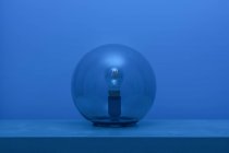 Moderna lampada spenta con lampadina all'interno sottile sfera di vetro trasparente al centro della mensola in camera blu al tramonto — Foto stock