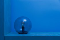 Moderno desligado luminária com lâmpada dentro fina esfera de vidro transparente no meio da prateleira no quarto azul ao entardecer — Fotografia de Stock