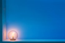 Lâmpada redonda elegante com luz amarela brilhante dentro da bola de vidro localizada na prateleira no quarto escuro com paredes azuis — Fotografia de Stock