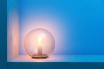 Стильна кругла лампа з яскраво-жовтим світлом всередині скляної кулі, розташованої на полиці в темній кімнаті з синіми стінами — стокове фото