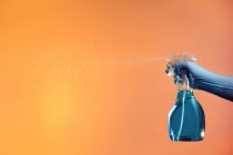 Анонимный человек с брызгами в пластиковой бутылке для дезинфекции поверхностей измельчающей жидкости на оранжевом фоне в студии — стоковое фото