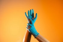 Anonymer Sanitäter in Einweg-OP-Handschuhen berührt Handgelenk auf orangefarbenem Hintergrund im Studio — Stockfoto