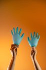 Persona senza volto con palloncini fatti di guanti medici che mostrano gesto della mano ondulante su sfondo arancione — Foto stock