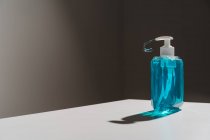 Пластиковая прозрачная бутылка с голубым жидким мылом, расположенным на белой поверхности, и тонким мыльным потоком, выходящим из белого дозатора — стоковое фото