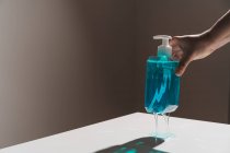 Bottiglia di plastica trasparente con sapone liquido blu situato sulla superficie bianca e sottile flusso di sapone che esce dal dispenser bianco — Foto stock