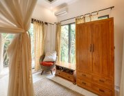 Interior del dormitorio con armario de madera y cómodo sillón de mimbre con cojines - foto de stock