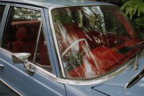 Винтажный автомобиль с красным антикварным интерьером припарковался под деревьями, отраженными в ветровом стекле — стоковое фото