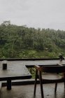 De cima do terraço com cadeiras de madeira e mesas perto de bungalow com telhado de palha cercado por plantas tropicais no dia sombrio em Bali — Fotografia de Stock
