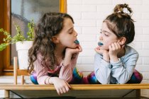 Two smiling sisters sticking out a blue tongue after eating a blue bubble gum — Stock Photo