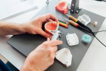 De cima de estudante de odontologia do sexo masculino cultura usando paquímetro para medir próteses dentárias enquanto trabalhava na mesa com ferramentas durante a aula — Fotografia de Stock