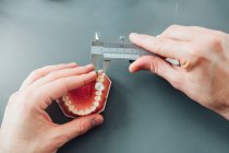Из выше урожая мужчина стоматолог студент, использующий суппортер для измерения зубного протеза во время работы за столом с инструментами во время занятий — стоковое фото