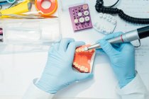 Von oben zugeschnittene anonyme Zahnarztpraktikantin in blauen Handschuhen, die während ihrer Arbeit im Labor zahnärztliche Operationen mit Bohrer-Schnitzguss durchführt — Stockfoto
