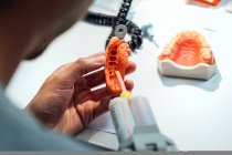 Vue de dessus du dos de l'orthodontiste mâle de la culture utilisant un équipement professionnel tout en travaillant avec un moulage dentaire dans un laboratoire moderne — Photo de stock