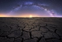 Tierra seca agrietada con sol poniente y estrellas en el cielo - foto de stock