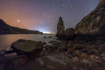 Paisaje nocturno de playa rocosa con cielo estrellado - foto de stock