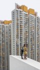 Fröhlicher erwachsener Mann und gesichtsloses Mädchen in buntem Kleid umarmen sich auf einem Betonschrägdach an den Fassaden gefleckter Wohnhochhäuser in Shek Kip Mei — Stockfoto