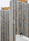 Maschio rilassato in abiti casual in posa sul tetto spiovente di cemento contro gli esterni di grattacieli residenziali con macchie grigie e gialle a Hong Kong — Foto stock