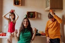 Доросла жінка і брати тримають барвистий перець і моляться в затишній кухні вдома — стокове фото