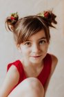Очаровательная девушка со свежей клубникой в булочках для волос улыбается и смотрит в камеру — стоковое фото