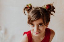 Menina adorável com morangos frescos em pães de cabelo sorrindo e olhando para a câmera — Fotografia de Stock