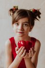Adorable niña con fresas en el pelo mostrando pimienta fresca y mirando a la cámara - foto de stock