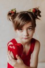 Entzückendes kleines Mädchen mit Erdbeeren im Haar zeigt frischen Pfeffer und blickt in die Kamera — Stockfoto