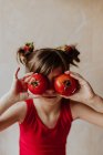 Nettes Mädchen hält frische Tomaten in der Nähe der Augen, während es in der Küche zu Hause Spaß hat — Stockfoto