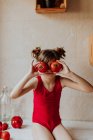 Linda chica manteniendo tomates frescos cerca de los ojos mientras se divierten en la cocina en casa - foto de stock