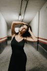 Молода жінка в елегантній чорній сукні стоїть в закритому підземному проході і мрійливо дивиться вгору — стокове фото
