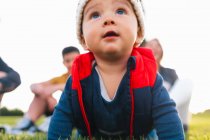 Cute ethnic toddler in warm clothes smiling while crawling on green meadow during family weekend in countryside — Stock Photo