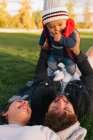 Coppia sdraiata sulla coperta sull'erba verde e con in braccio un bambino carino in caldo mentre riposa durante il fine settimana nel parco — Foto stock