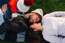 Dall'alto di giovane coppia allegra con bambino piccolo sdraiato su plaid su erba verde e godendo il tempo insieme mentre trascorrono la giornata nel parco — Foto stock