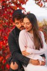 Heureux jeune homme et femme embrasser tout en étant assis sur le banc près de l'arbre d'automne coloré dans le parc — Photo de stock