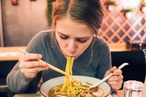 Junge Frau isst mit Essstäbchen und Löffel leckeren Ramen, während sie am Tisch in einem japanischen Restaurant sitzt — Stockfoto