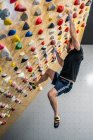 From bellow strong male athlete in sportswear climbing on colorful wall during workout in modern climbing center — Stock Photo