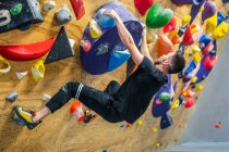 Dal soffio di irriconoscibile forte atleta maschile in abbigliamento sportivo arrampicata su parete colorata durante l'allenamento in ragazzo moderno — Foto stock