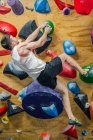 From bellow unrecognizable strong male athlete in sportswear climbing on colorful wall during workout in modern climbing center — Stock Photo