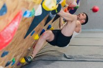 Desde la vista lateral de fuelle de fuerte atleta masculino en ropa deportiva escalada en la pared colorida durante el entrenamiento en chico moderno - foto de stock