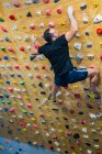 From bellow unrecognizable strong male athlete in sportswear climbing on colorful wall during workout in modern guy — Stock Photo