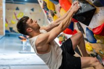 Вид збоку сильного спортсмена-чоловіка в спортивному одязі, сходження на барвисту стіну під час тренування в сучасному хлопці — стокове фото