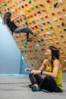 Seitenansicht einer zufriedenen Athletin, die in Lotus-Pose auf dem Boden sitzt, während sie beim Klettern im Fitnessstudio lächelt und wegschaut — Stockfoto