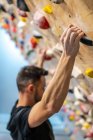 Вид збоку розмитого анонімного сильного спортсмена-чоловіка в спортивному одязі, сходження на барвисту стіну під час тренування в сучасному хлопці — стокове фото