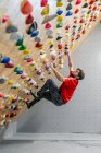 From bellow side view of strong male athlete in sportswear climbing on colorful wall during workout in modern guy — Stock Photo