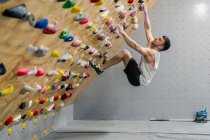 From bellow side view of strong male athlete in sportswear climbing on colorful wall during workout in modern guy — Stock Photo