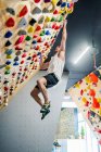 Side view from below of young man in active wear holding grips tightly while hanging in air during climbing training in gym — Stock Photo