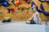 Seitenansicht eines muskulös lächelnden Mannes und einer Frau, die auf dem Boden sitzen und weglächeln, während sie in der Kletterhalle trainieren — Stockfoto