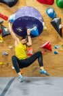 Сильний молодий чорноволосий жіночий альпініст в активному одязі посміхається, повісившись на великому руків'ї скелелазної стіни в спортзалі — стокове фото