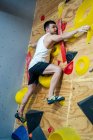 С нижней стороны вид сильного спортсмена в спортивной одежде, лазающего по красочной стене во время тренировки у современного парня — стоковое фото