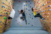 Vue latérale d'un jeune groupe d'alpinistes forts, hommes et femmes, s'entraînant au mur dans une salle de gym moderne — Photo de stock